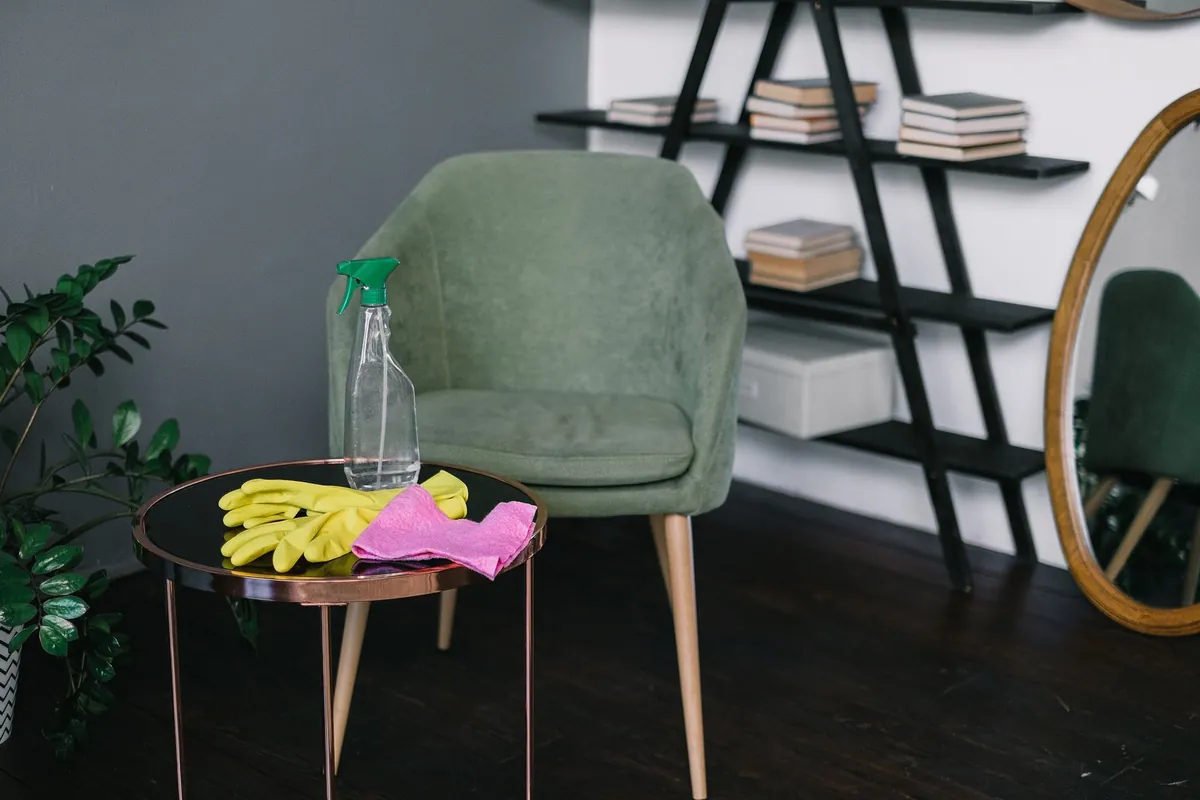 Yellow cleaning gloves, a spray bottle and a pink cloth on a side table in a tidy living room