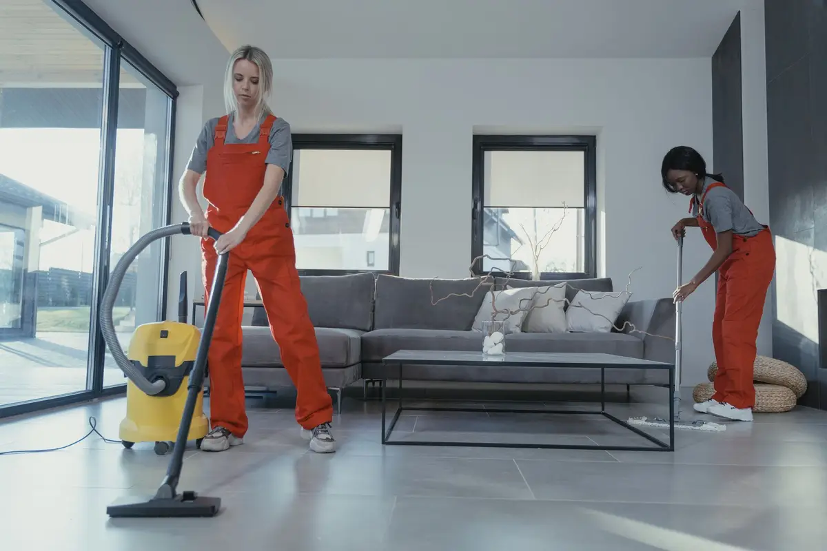Two cleaners in red coveralls vacuuming and sweeping a modern living room